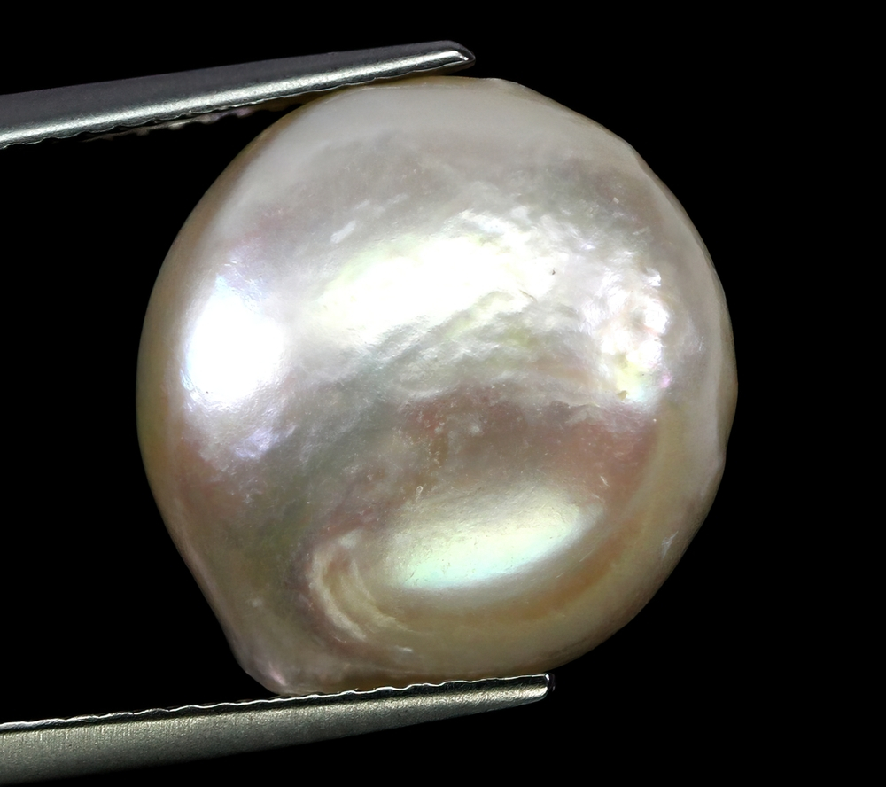 Perle naturelle sur fond noir illustrant le lustre et l'orient d'une gemme précieuse